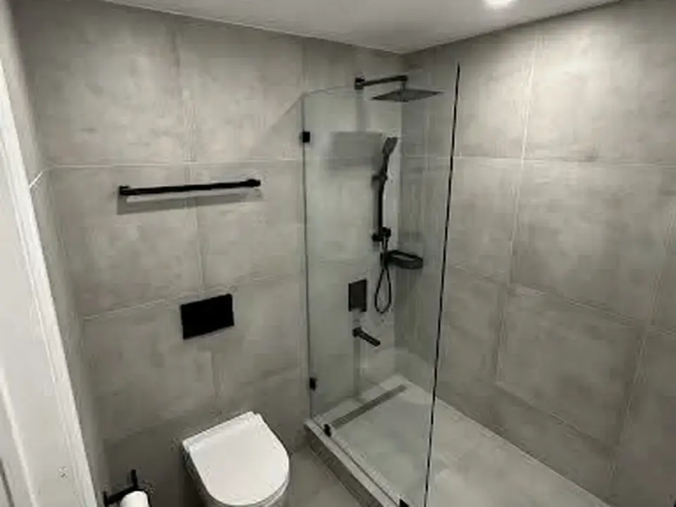 Finished bathroom with large-format grey tile, a glass shower, and wall-mounted toilet