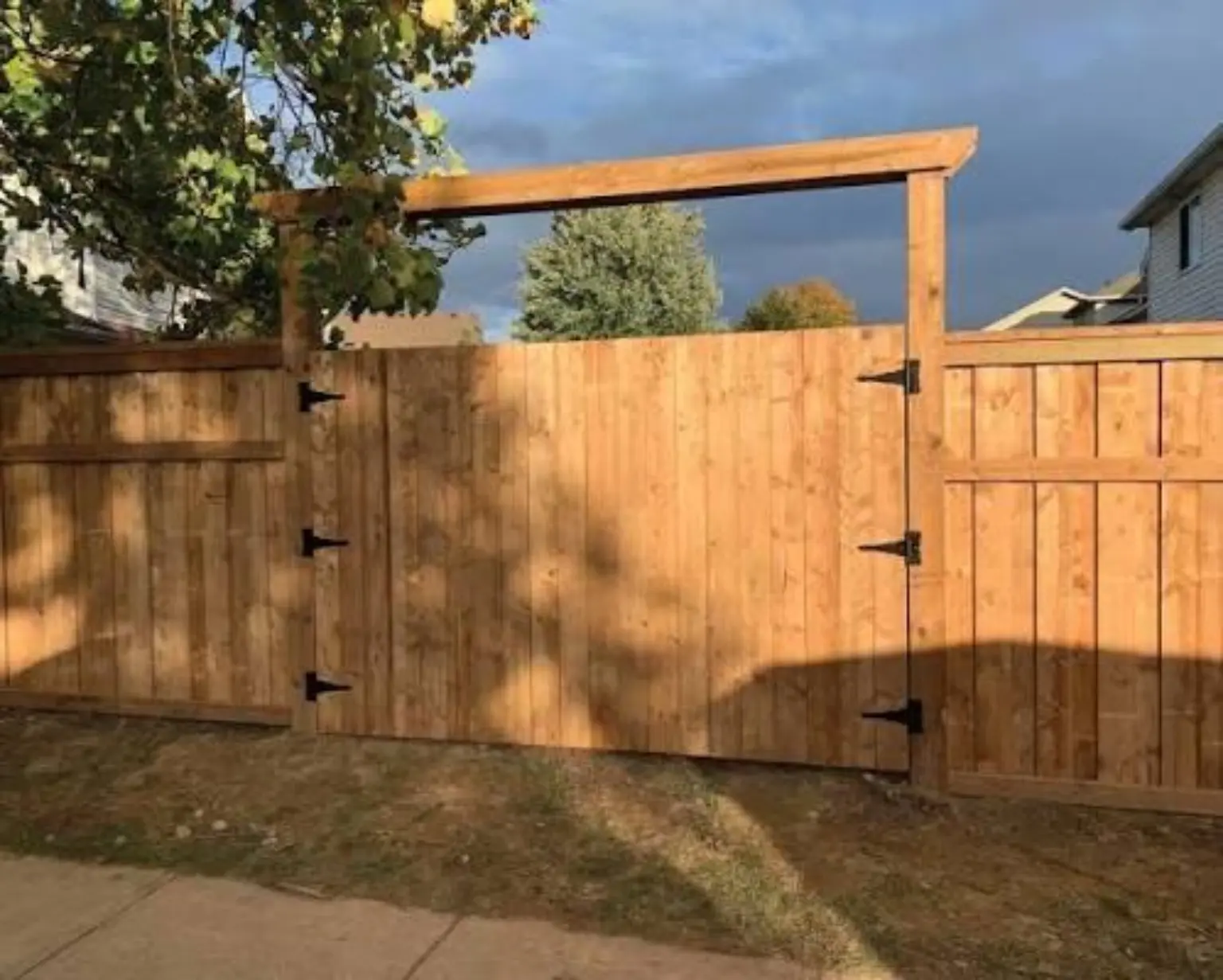 Wide cedar double gate with black hinges and an overhead brace