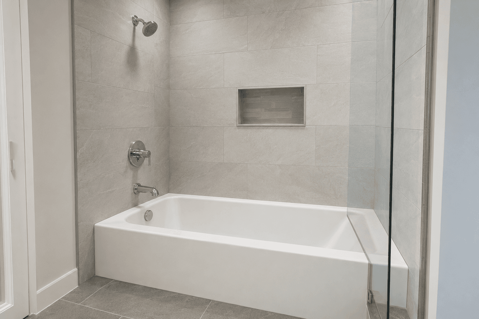 White alcove tub with pale tile walls, shower fixtures, and a glass panel