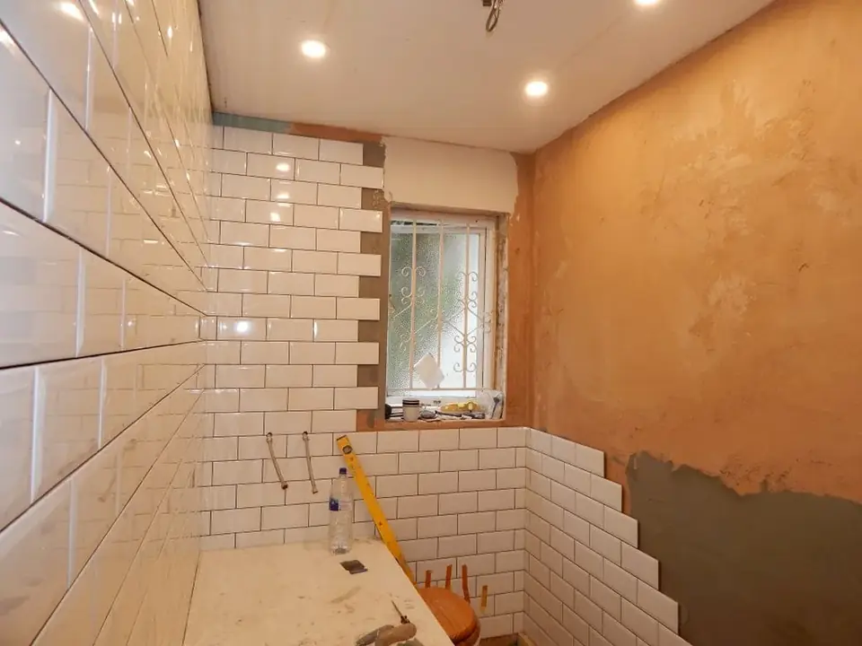 Bathroom renovation in progress with white wall tile and recessed lighting