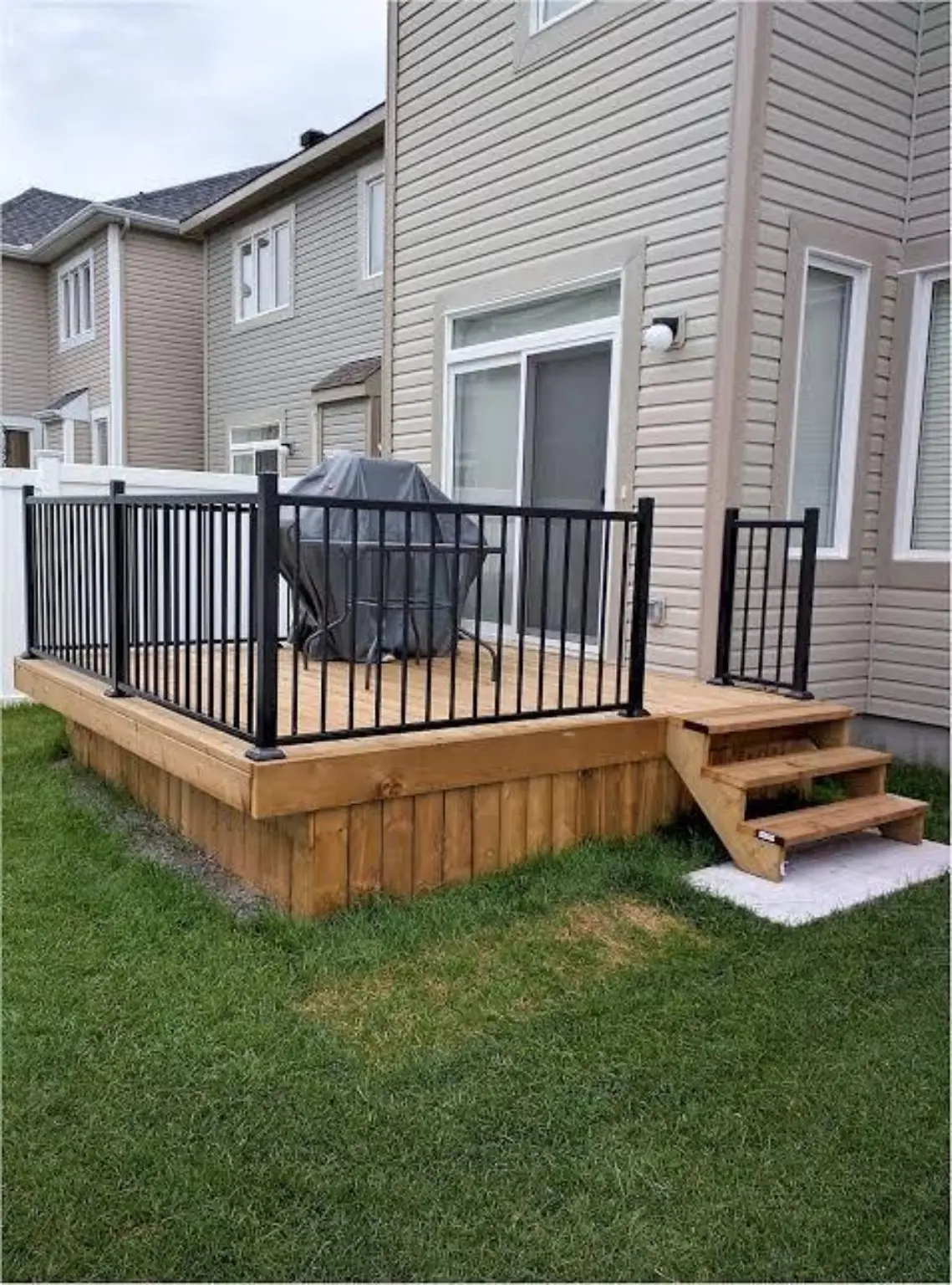 Compact backyard deck with black railings, wood skirting, and steps