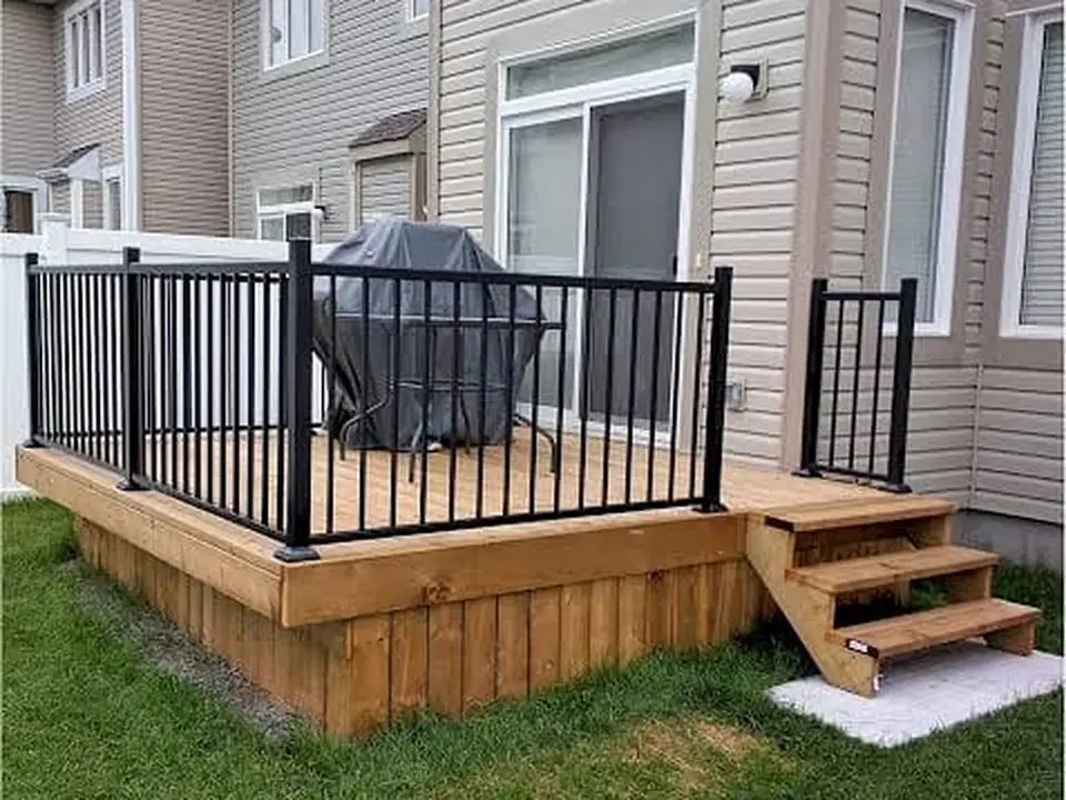 Finished backyard deck with black metal railings and wood skirting