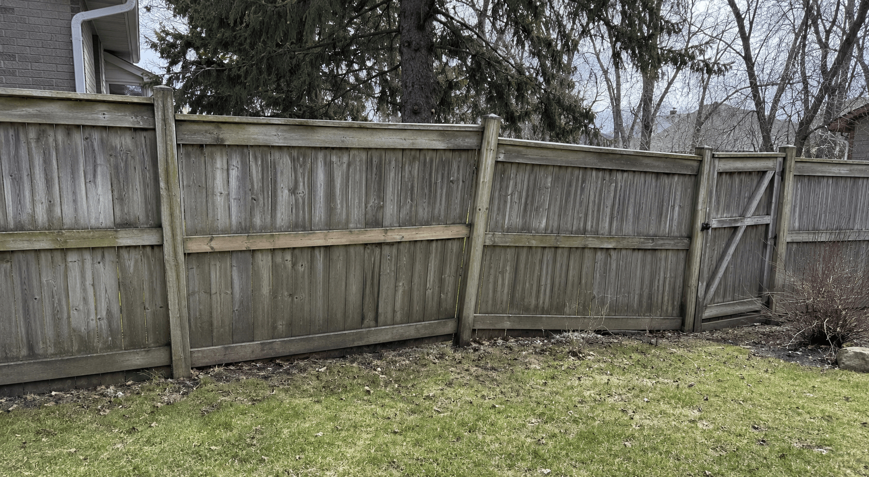 Weathered wood fence leaning between backyard posts