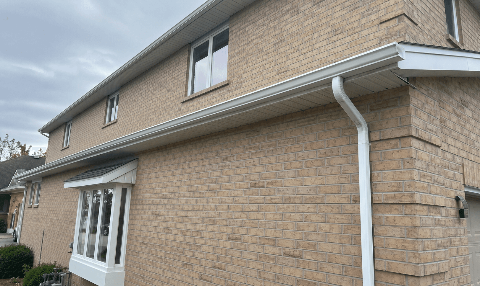 White eavestrough and downspout installed along a brick home