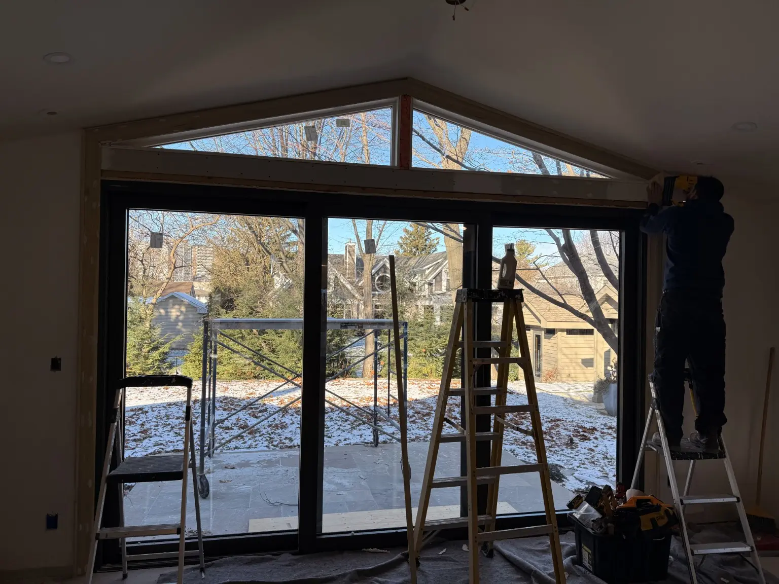 Oversized black patio-door system with a peaked transom during finishing