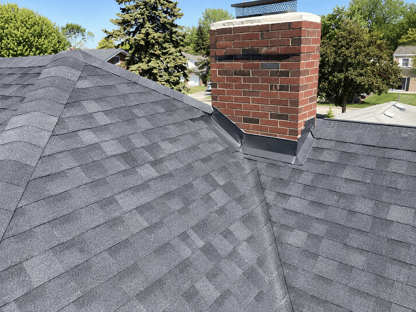 Asphalt shingles and metal flashing surrounding a brick chimney