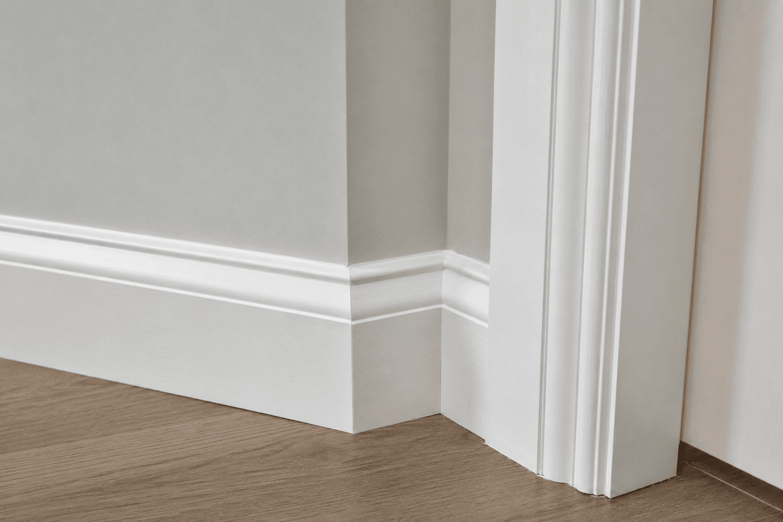 Close view of white baseboard meeting a fluted doorway casing