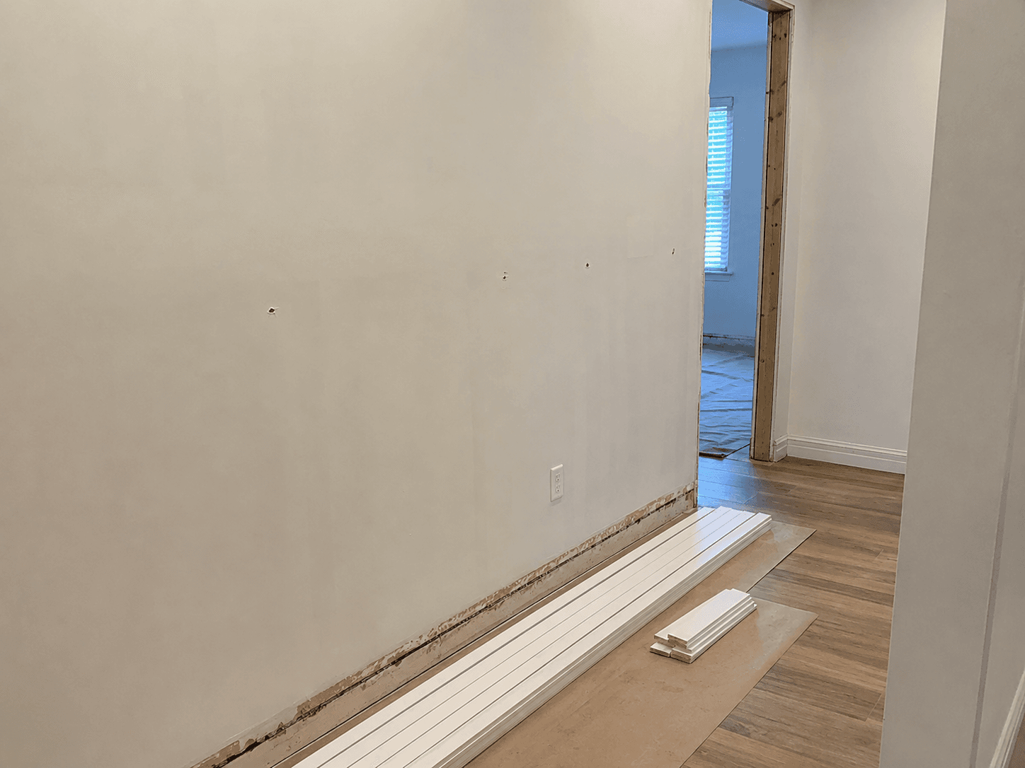 Interior wall with removed baseboard and new trim pieces ready for installation